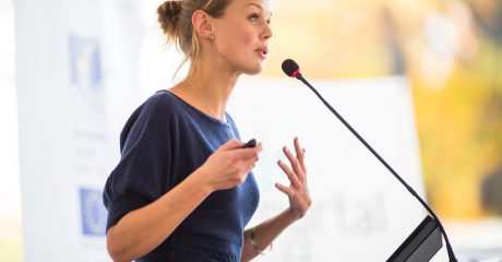 Eine Frau steht vor einem Rednerpult und spricht in ein Mikrofon