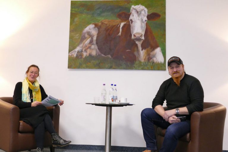 Gespräch zwischen zwei Personen mit einem gemalten Bild von einer Kuh an der Wand